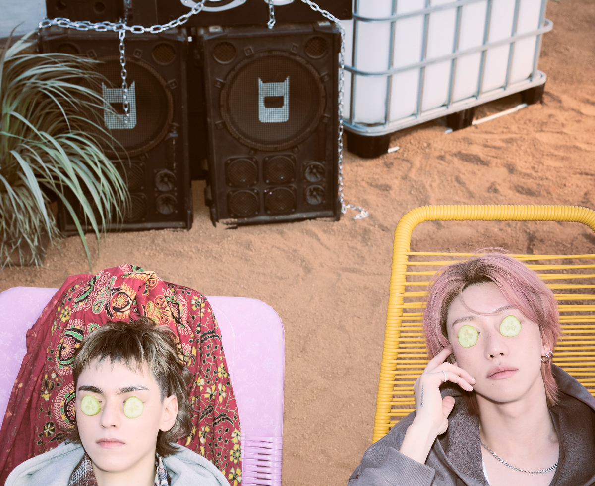 Vernon & the 8 on beach chairs, eyes covered with cucumbers, as chained speakers sit in the background on the sand