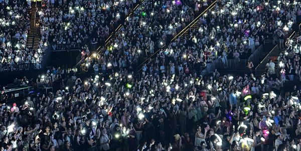A crowd of fans with lightsticks lit up, predominantly in white but with different pockets of color as well.