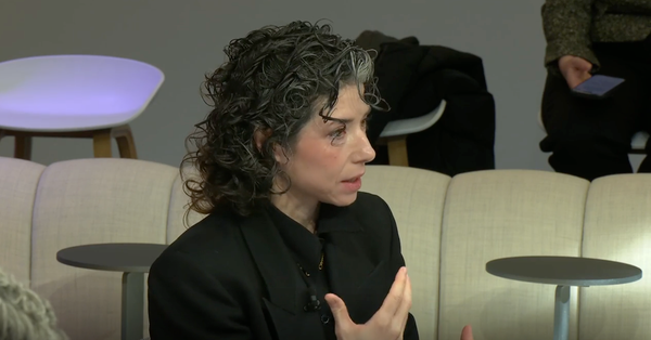 Whittaker with black curly hair wearing a black suit, gesturing as she speaks.