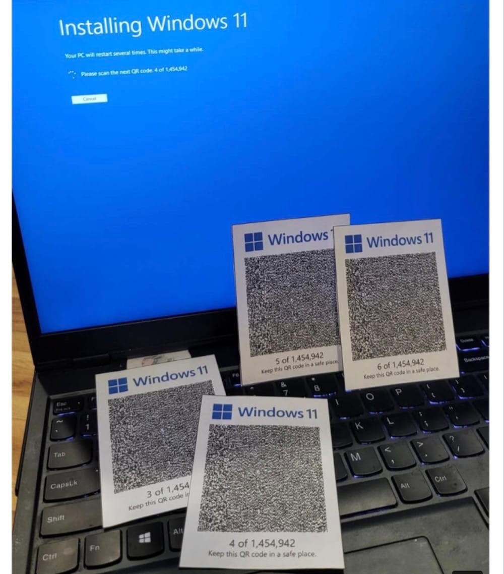 The image shows a laptop with a blue screen displaying the message "Installing Windows 11." The screen also instructs the user to scan the next QR code, with a number indicating the sequence. Four QR code cards are placed on the laptop's keyboard, each labeled "Windows 11" and numbered from 3 to 6 out of 1,454,942. 