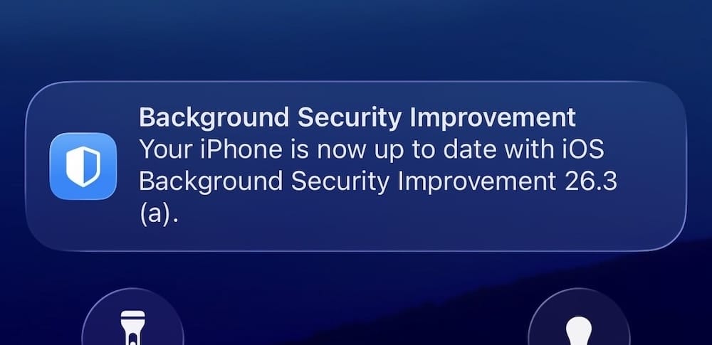 a screenshot of a blue iPhone display with a notification, saying: "Background Security Improvement Your iPhone is now up to date with iOS Background Security Improvement 26.3 (a)."