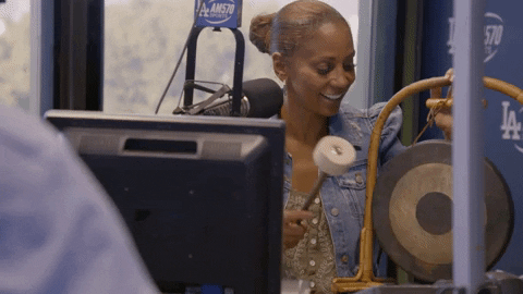 an animated GIF of a radio show presenter in front of a microphone, hitting a gong with a mallet.