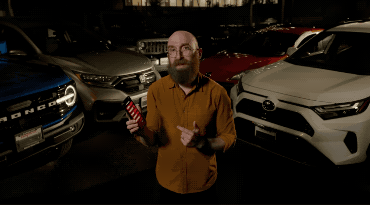 an animated GIF of Andy Greenberg, tapping a button on a phone app, then all of the cars surrounding him lighting up with their headlights and indicator lights.