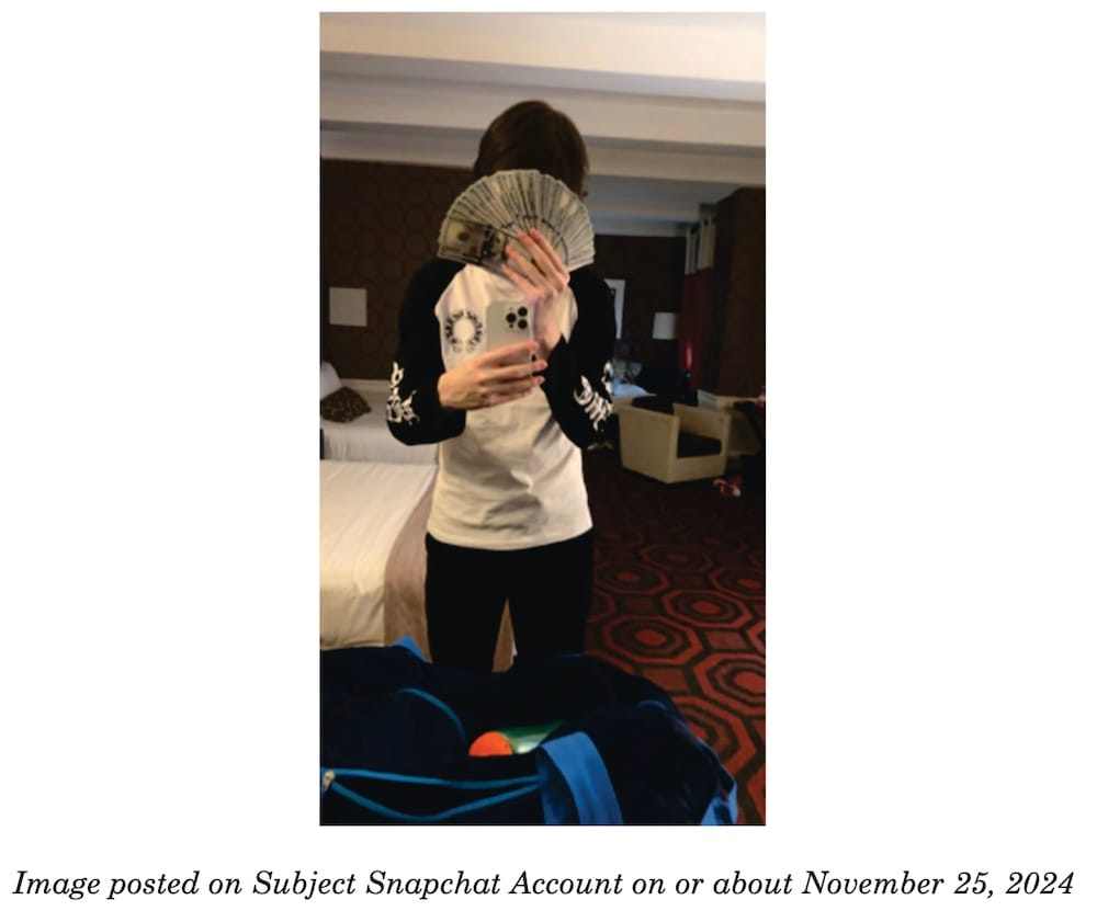 a photo from Peter Stokes' indictment, showing Stokes (allegedly) holding a fan of cash in front of his face while in a hotel room in Bangkok in 2024.