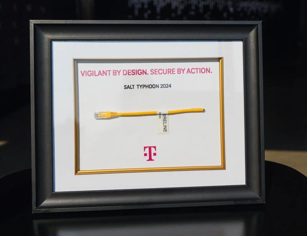 a photo of a yellow cable that has been snipped in half, framed, that reads: "Vigilant by design, secure by action," following the Salt Typhoon attack of 2024.