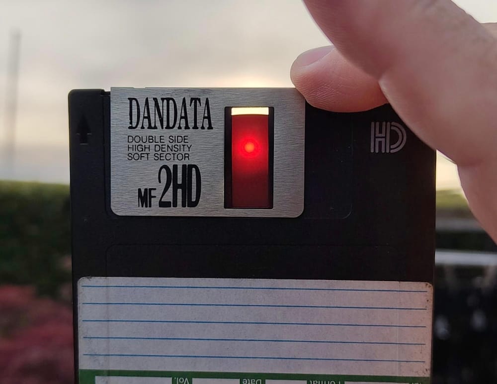a photo of the sun appearing as a bright red dot through the thin film of a floppy disk held up to the sky during a solar eclipse.