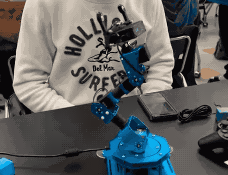 an animated GIF of a small blue desktop robot arm moving its arm towards the power cable that it's plugged into, and then pulling it out, immediately cutting the robot's power supply, freezing it on the table.