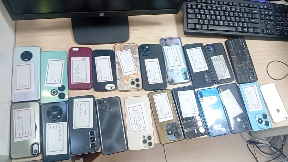 a photo of a bunch of seized phones on a desk, with notes on each one describing what they are used for in the scams.