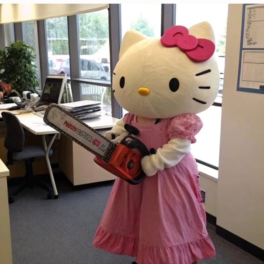 A person in a full Hello Kitty body suit wearing a pink dress, and holding a chainsaw in what appears to be an office.