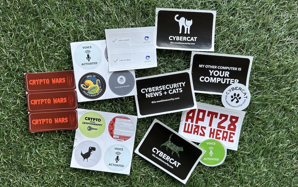 A photo of a selection of stickers featuring ~this week in security~'s cyber cat motifs and other stickers..