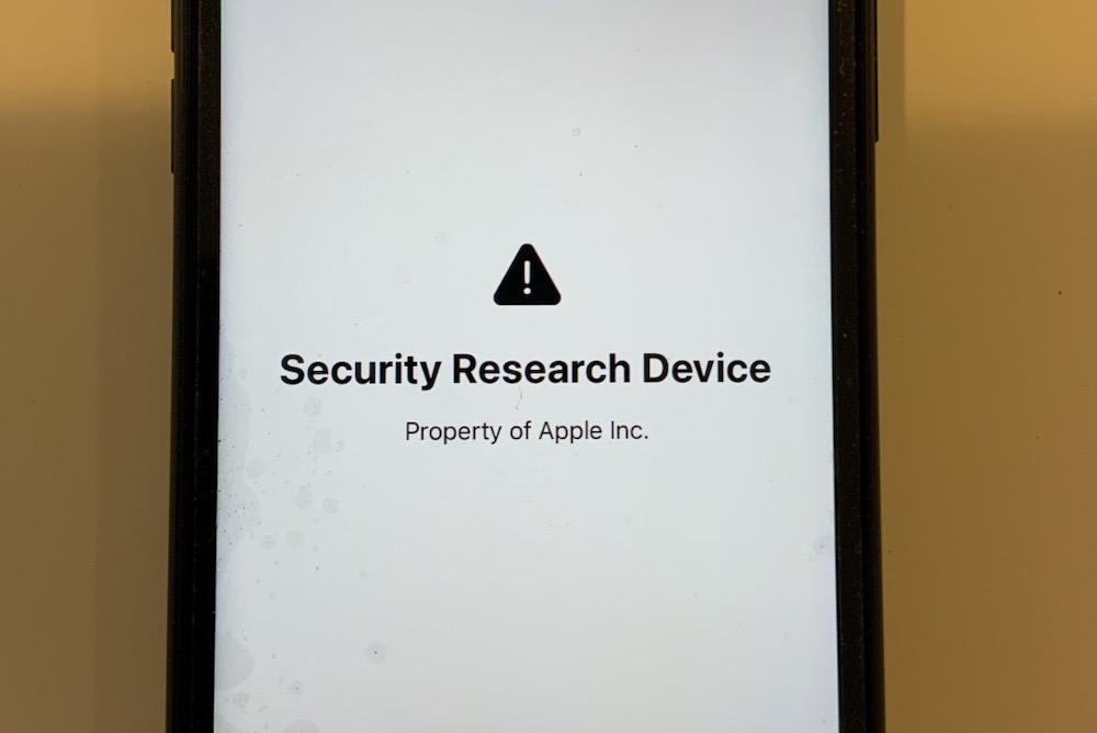 A photo of an iPhone on a yellow background, which reads on the display: "Security Research Device. Property of Apple Inc." with a triangle warning symbol.