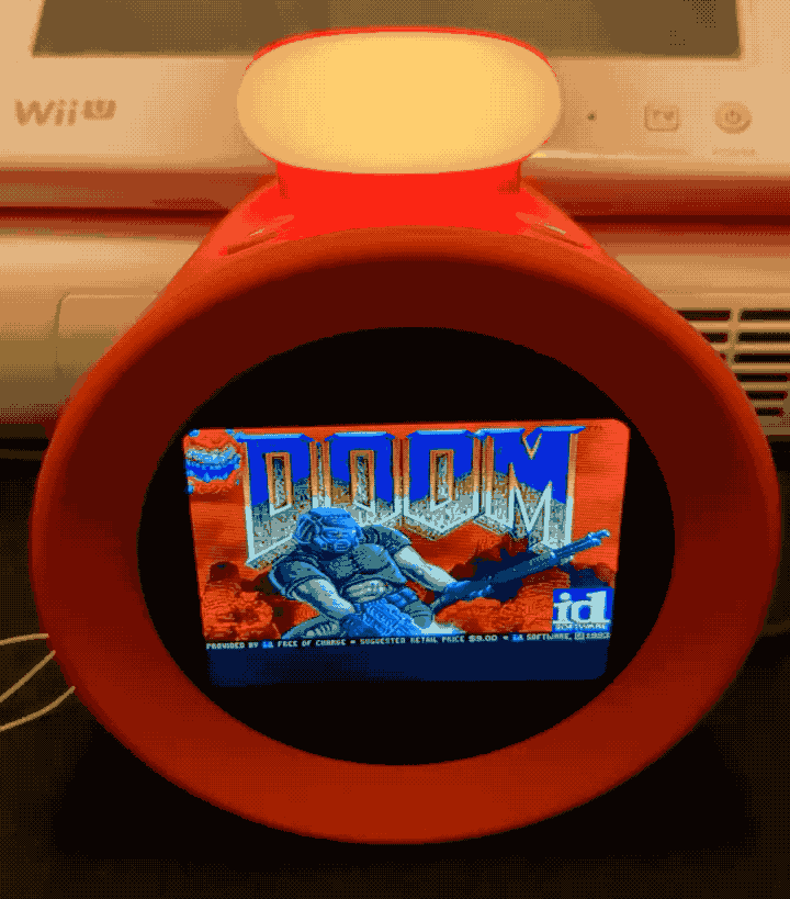 A Nintendo Alarmo on a desk, with a small LCD display that's running the first-person shooter, Doom.