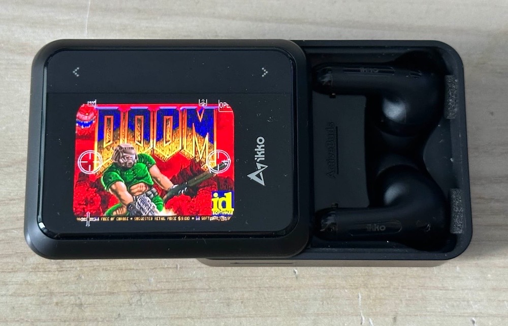 A photo of a pair of ikko earbuds in a box, which features a small LCD display, which has been loaded with "Doom."