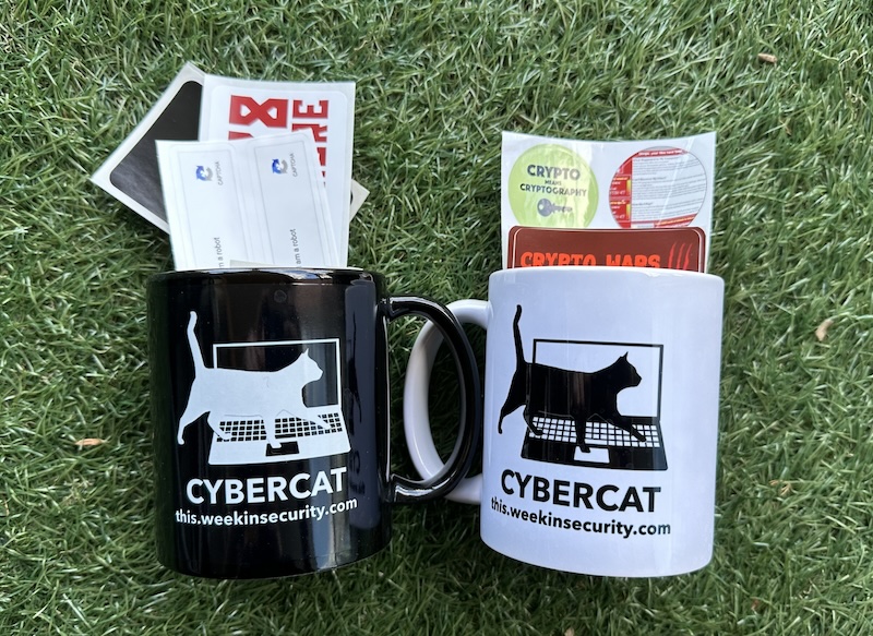 A selection of stickers in two "this week in security" mugs, one in black and the other in white, on a green grassy background.