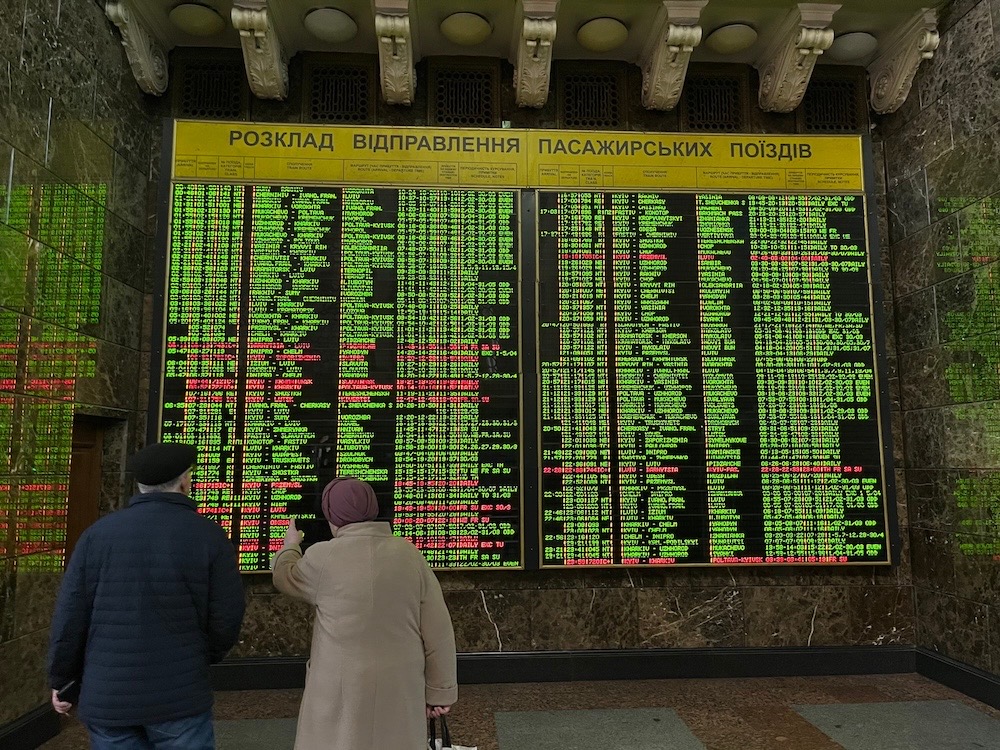 A photo from Kyiv's central railway station, showing a digital departure board (in Ukrainian) with green departures and red text for delays.