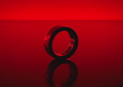 an Oura ring stood up on its side, against a red lit backdrop. 