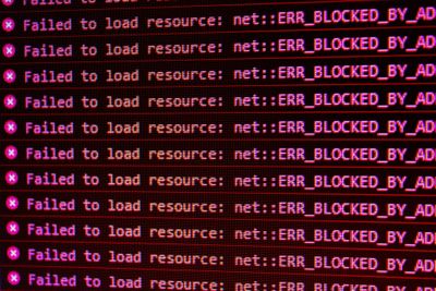 a screenshot of red text from a browser console log, which reads "Failed to load resource: net::ERR_BLOCKED_BY_AD" signifying the use of an ad-blocker.