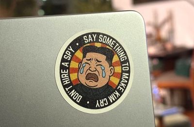 a photo on the back of my laptop with a sticker, featuring a cartoon of Kim Jong Un crying, with the words: "Don't hire a spy, say something to make Kim cry." I made this sticker!