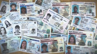 a photo of a collection of U.S. fake driver's licenses scattered across a table randomly