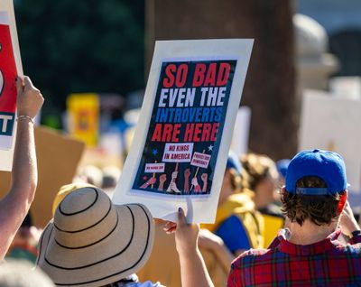 a photo of protesters holding signs at a No King's rally in the U.S. in 2025 — one sign says, "So bad even the introverts are here."