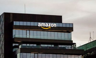 a photo of Amazon's logo on a building in a background, with blue-tinted windows, and a grey-ish cloud overhead.
