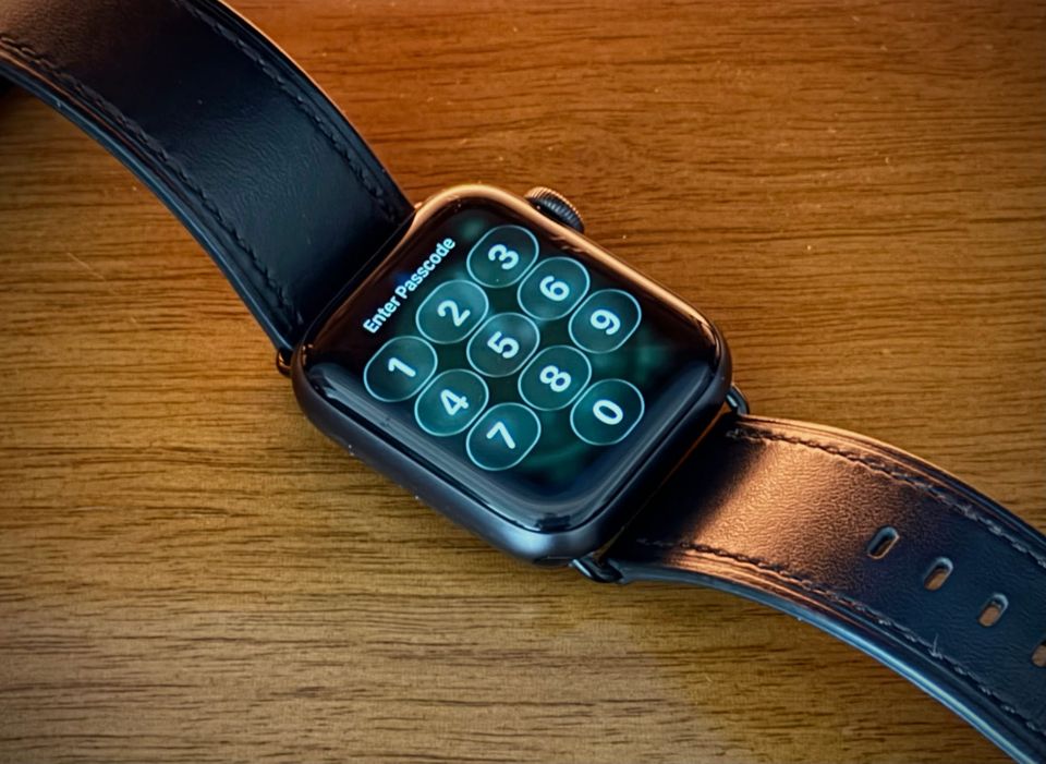 a photo of an Apple Watch showing its pascode lock-screen on a wooden table with an orange light nearby.