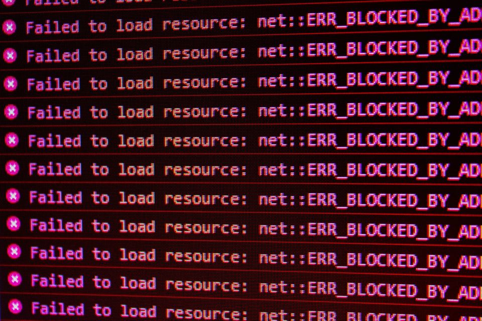 a screenshot of red text from a browser console log, which reads "Failed to load resource: net::ERR_BLOCKED_BY_AD" signifying the use of an ad-blocker.