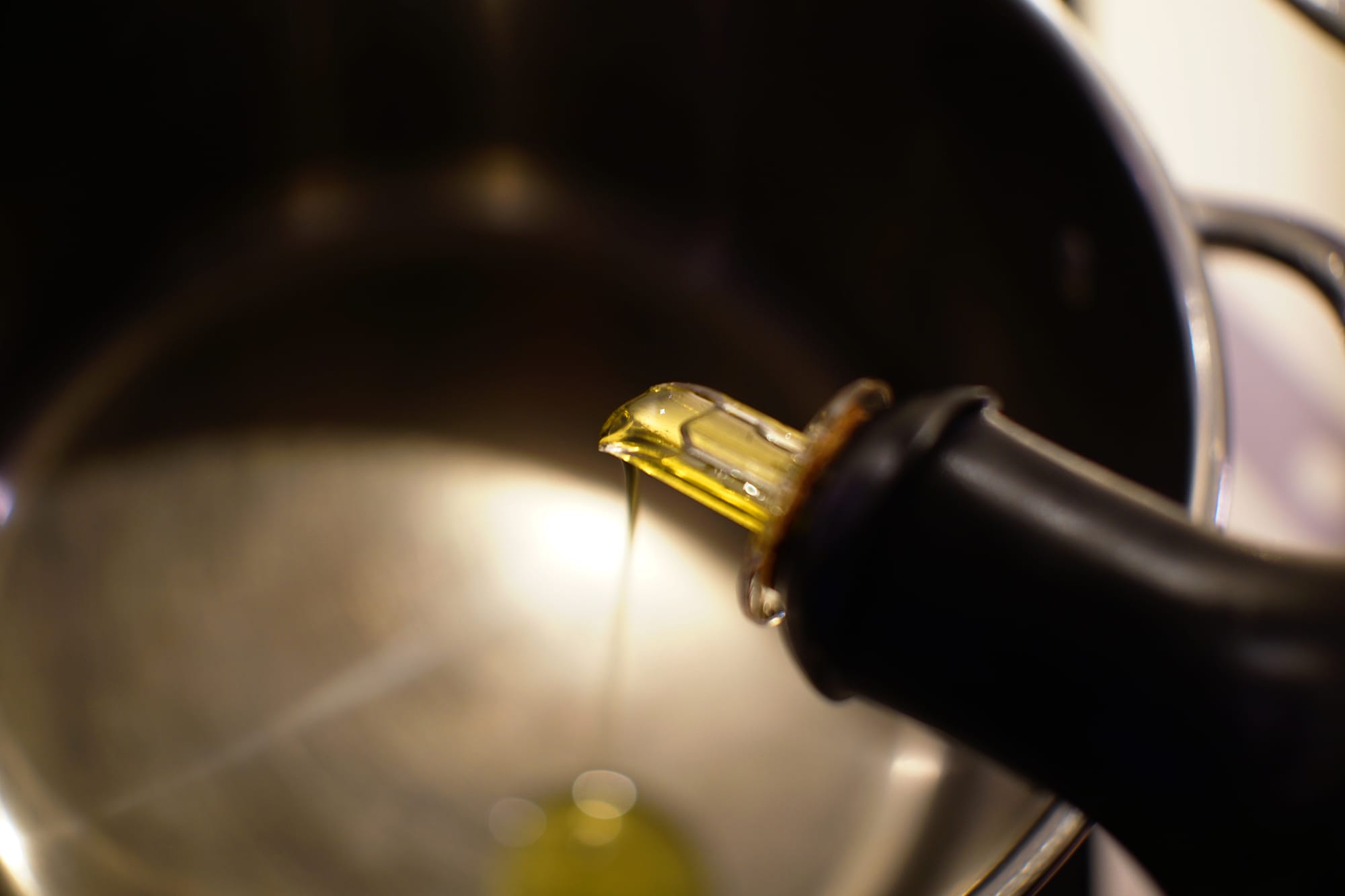 Olive oil being poured from a black bottle into the pot.