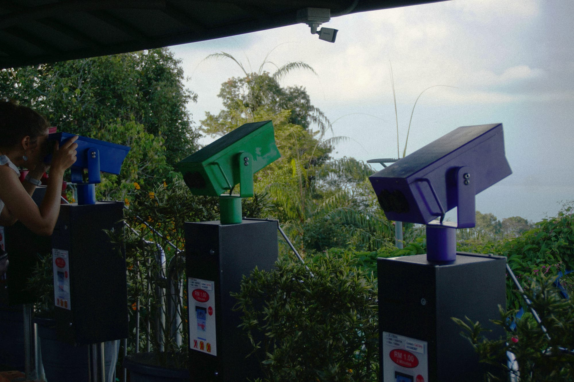 Three mounted binoculars, one purple, one green, and one blue, overlooking from Penang Hill.