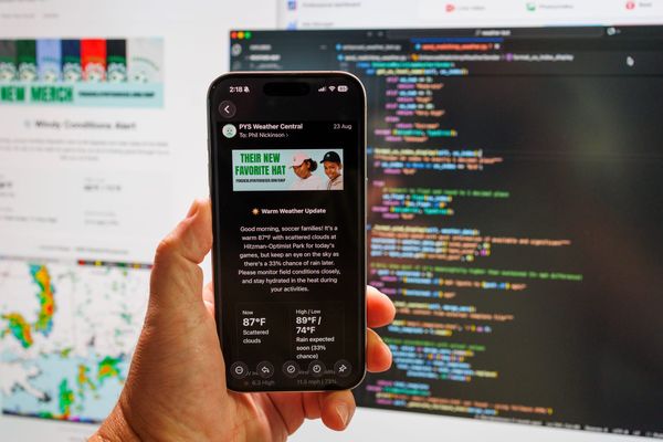 A Weatherbot email seen on an iPhone being held in front of the code on a computer screen.