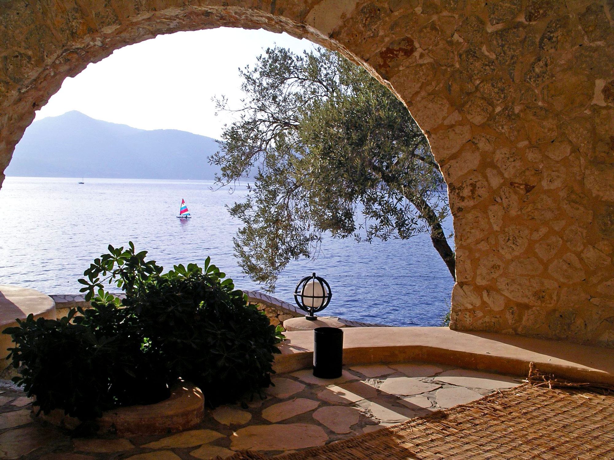 View of a small sailboat far off in the sea through an arched opening in a beautiful manmade cave 
