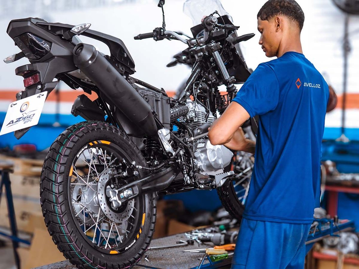 Motocicleta Avelloz AZ1 branca e preta estacionada em frente a um galpão industrial, com outra moto em segundo plano