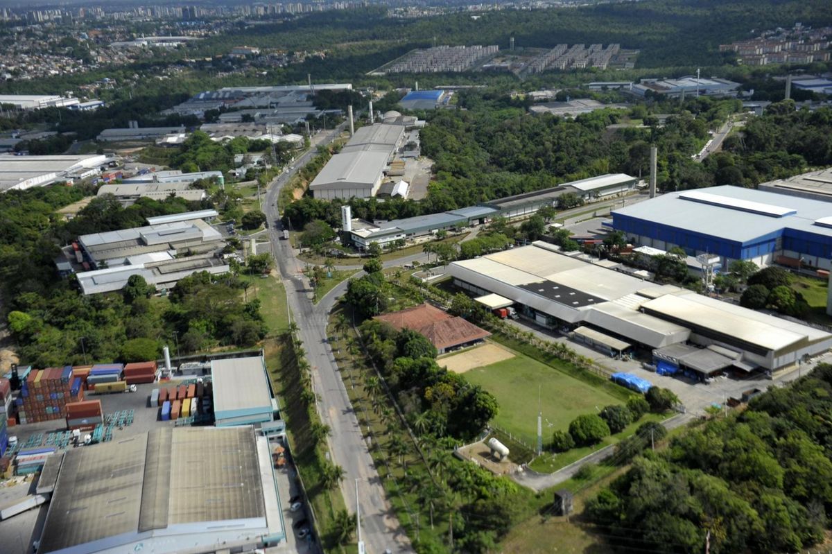 Vista aérea do Distrito Industrial de Manaus, com galpões e indústrias em meio à vegetação, sob céu azul.