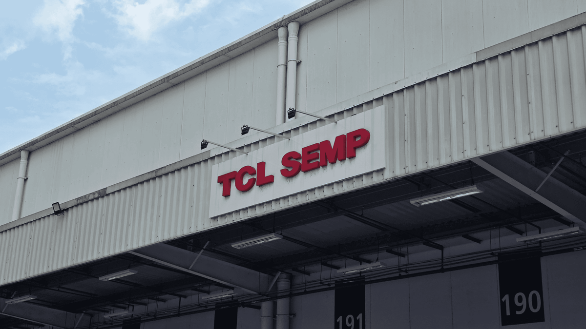Fachada de um prédio industrial com o letreiro vermelho "TCL SEMP" em destaque, sob um céu nublado