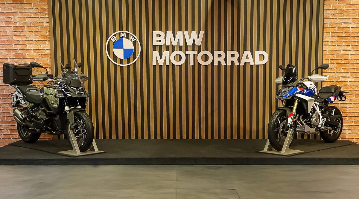 Duas motocicletas BMW Motorrad, uma preta e uma branca com detalhes azuis e vermelhos, em exposição com o logo da marca ao fundo