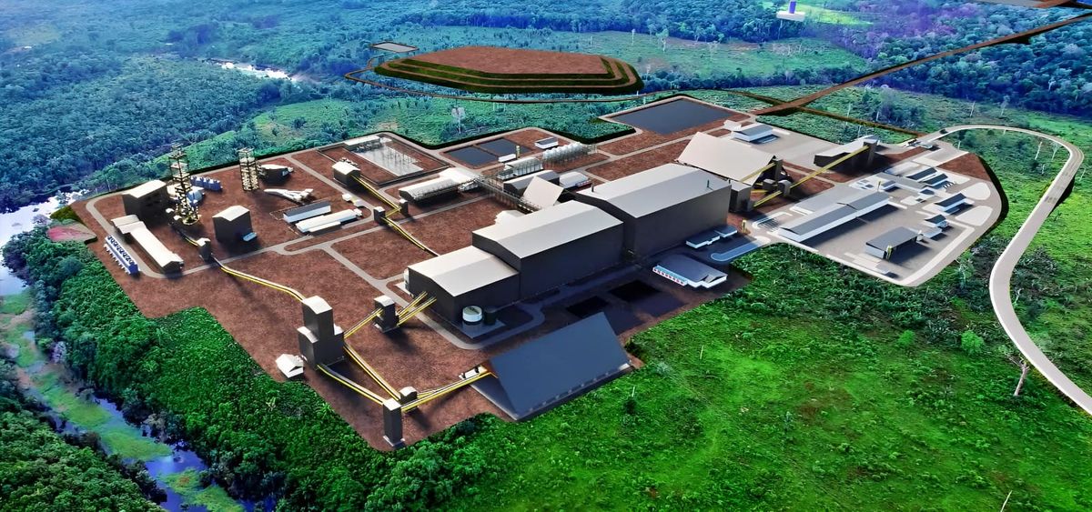 Vista aérea de uma grande área industrial com edifícios cinzas e marrons, cercada por vegetação densa e um rio sinuoso