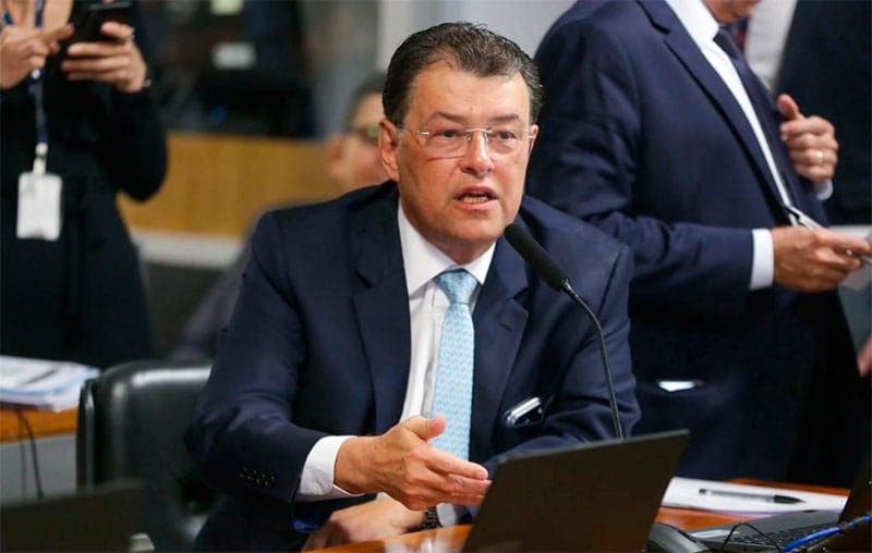 O senador Eduardo Braga fala ao microfone durante sessão no Senado, vestindo terno azul e óculos.