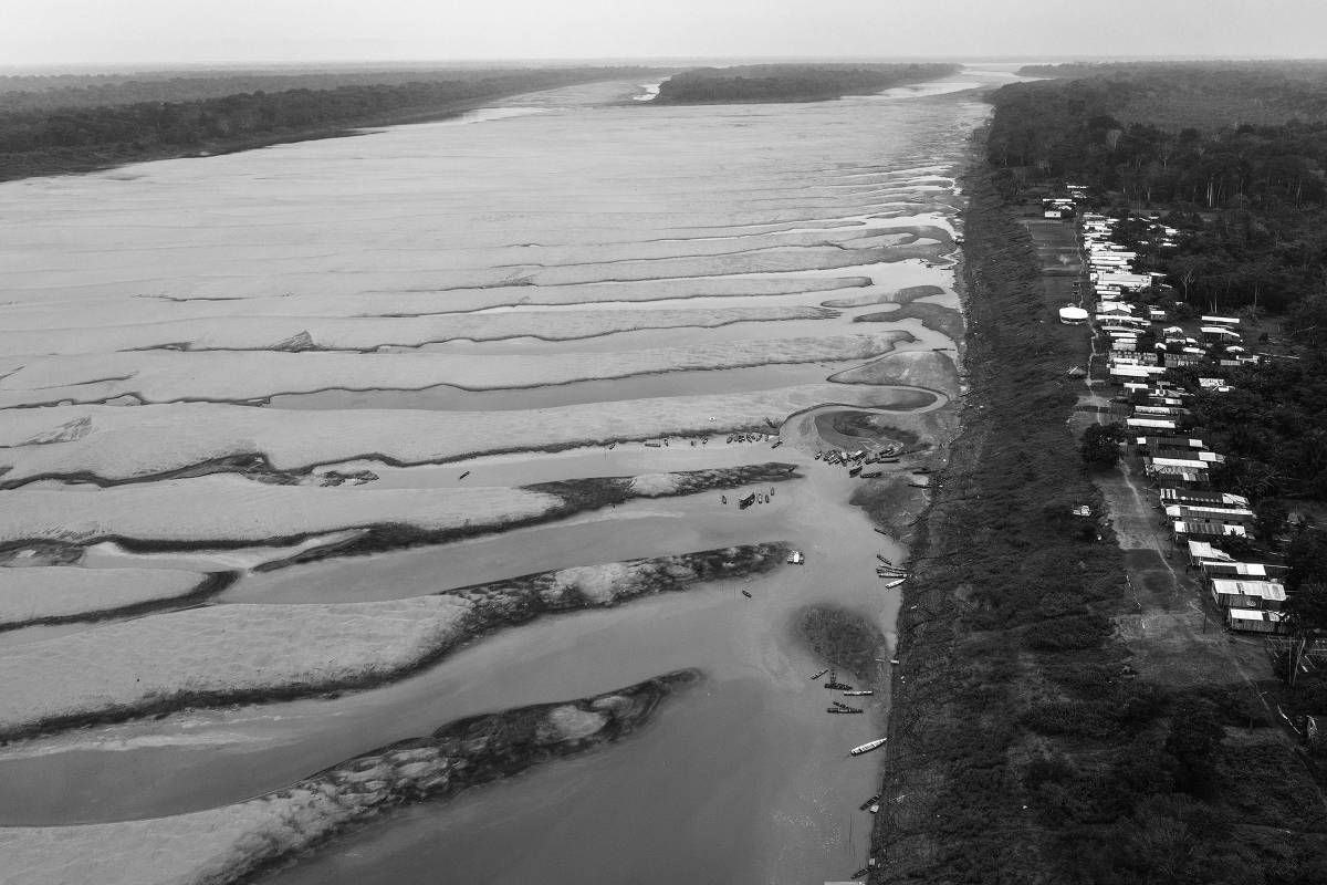 Vista aérea do leito seco do rio Solimões, com bancos de areia expostos e pequenas embarcações, ao lado de uma comunidade