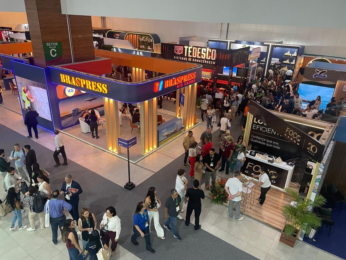 Pessoas em um evento de negócios, com stands e banners ao fundo, representando uma feira de logística