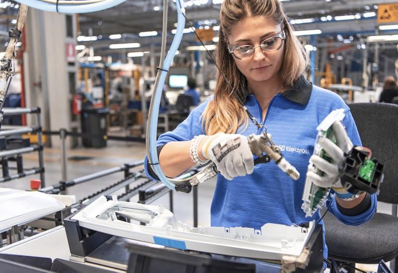 Linha de montagem de eletrodomésticos com trabalhadores e robôs, destacando a produção industrial moderna