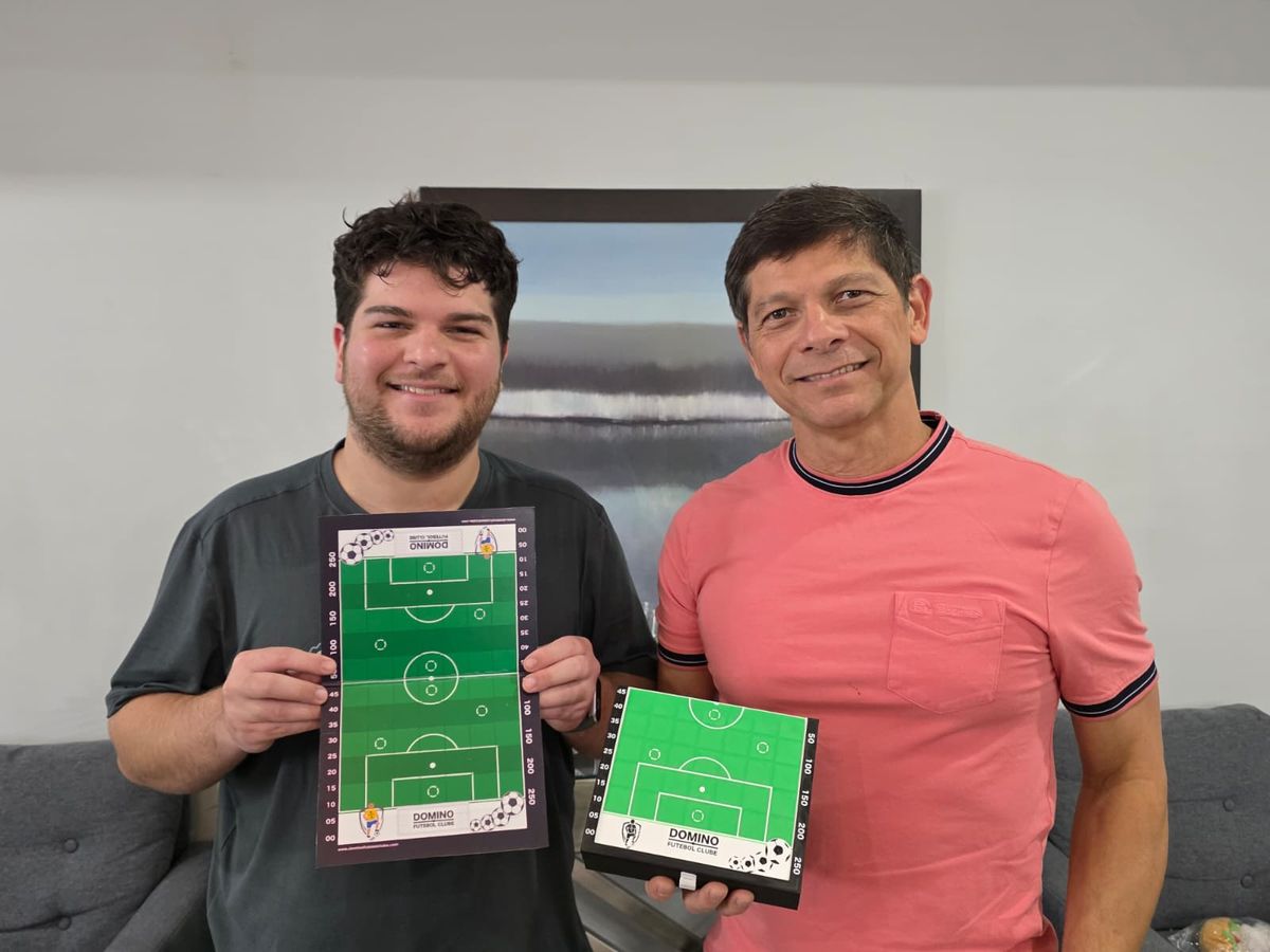 Heimar Pinheiro de Oliveira e Heriam Brito de Oliveira, pai e filho, segurando o tabuleiro do jogo Dominó Futebol Clube