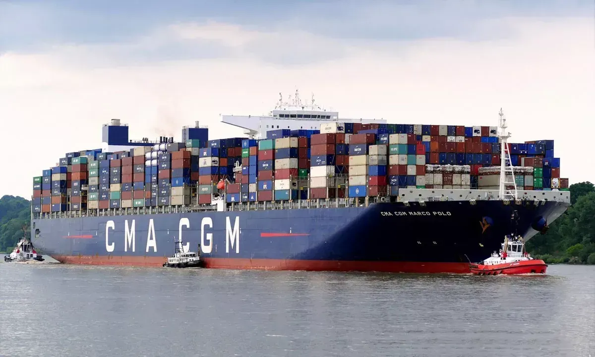 Contêineres empilhados em um terminal portuário, com um navio de carga ao fundo, simbolizando o transporte marítimo