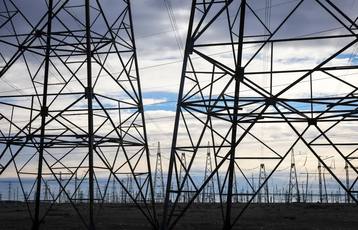 Silhueta de torres de transmissão de energia elétrica em campo aberto, com céu nublado ao fundo
