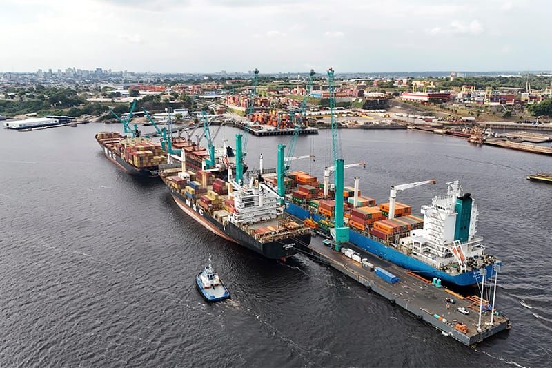 Navios de carga atracados no terminal portuário do Super Terminais, em Manaus, com diversos contêineres e guindastes.