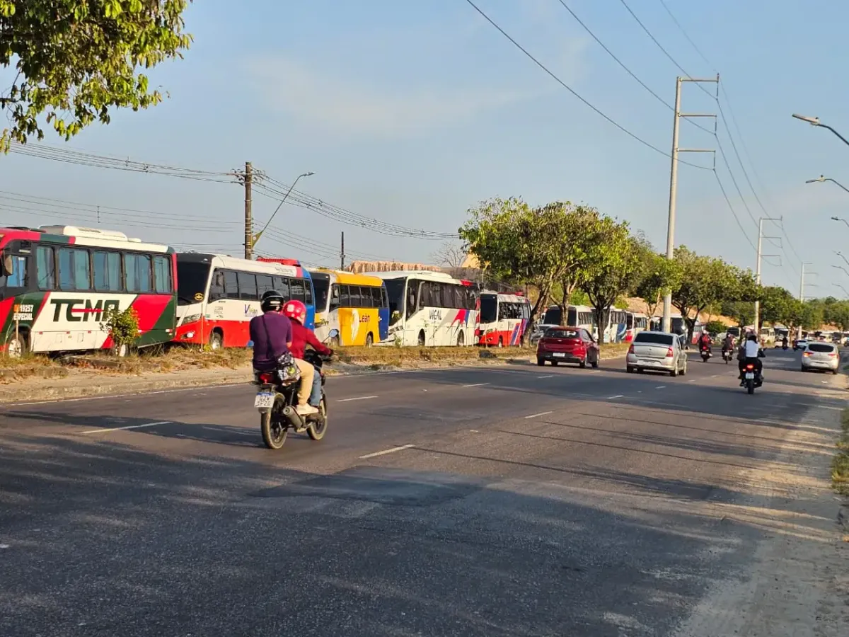 Ônibus de transporte especial parados na lateral de uma via, com carros e motocicletas em movimento na pista, em Manaus