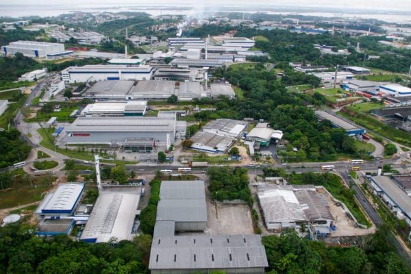 Vista aérea de galpões industriais cercados por vegetação no Polo Industrial de Manaus.