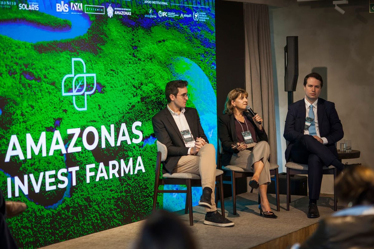 Isabel Reis fala em microfone sentada em painel ao lado de dois homens durante o evento Amazonas Invest Farma em São Paulo.