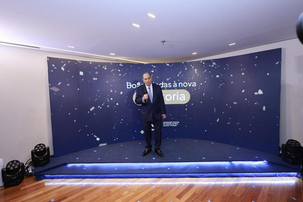 José Roberto Tadros discursa em um palco com fundo azul e a frase Boas-vindas à nova diretoria em Brasília.