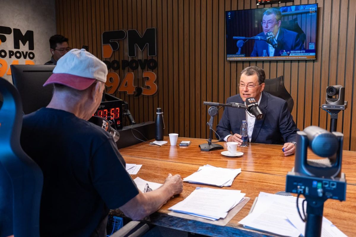 Senador Eduardo Braga concede entrevista em estúdio de rádio, sentado à mesa com microfone e papéis à frente.