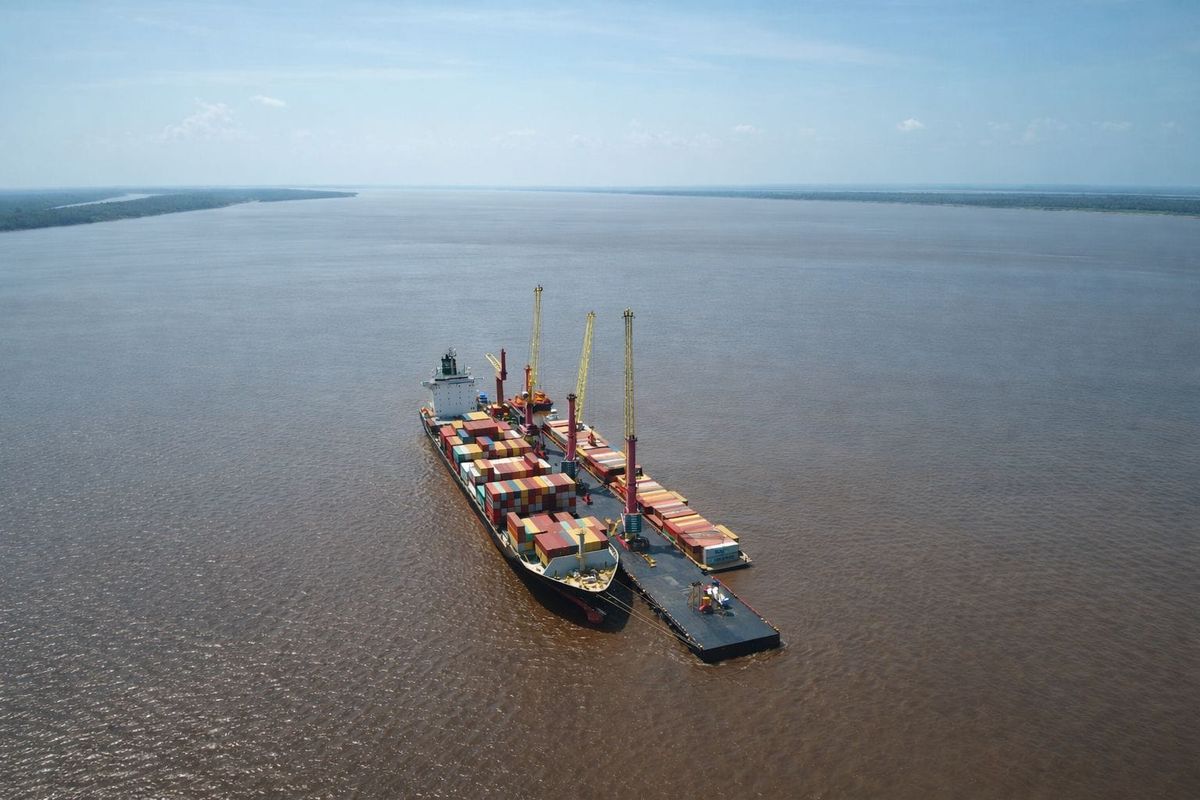 Navio cargueiro atracado em balsa com guindastes no meio do rio Amazonas durante operação de transbordo de contêineres.